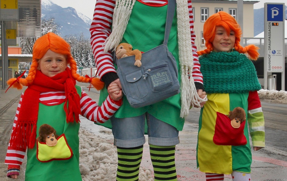 Tripple Pippi Langkous cosplay, volwassene en twee kinderen. Gestreepte truien en kousen en rode pruiken met brede vlechten.