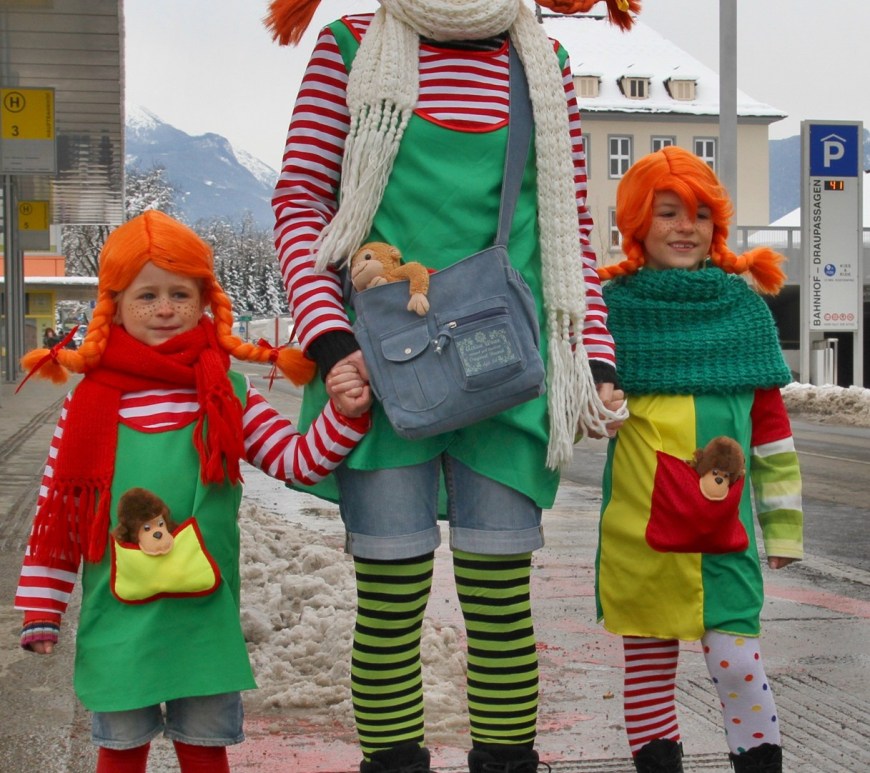 Tripple Pippi Langkous cosplay, volwassene en twee kinderen. Gestreepte truien en kousen en rode pruiken met brede vlechten.