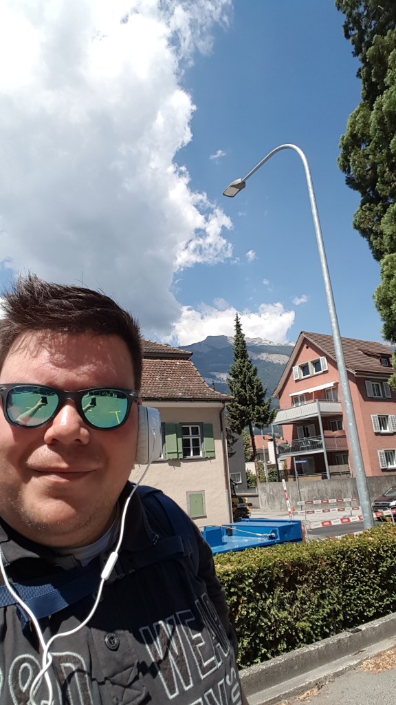 Ik in Chur in Zwitserland (denk ik). Op de achtergrond typische huisjes en een Alp.