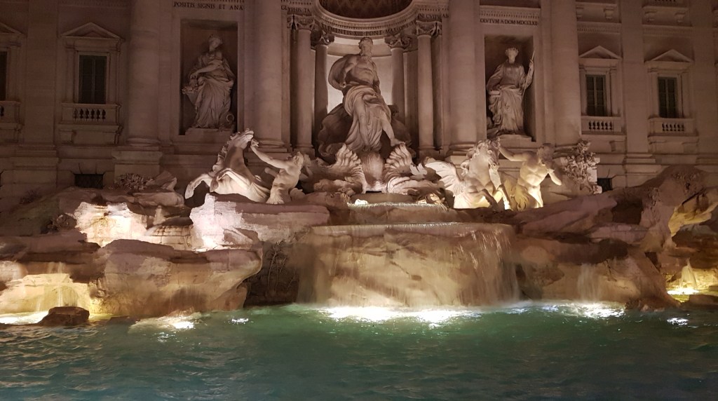 Beroemde Trevifontein in Rome, midden in de nacht. De stenen beelden op de fonteint worden verlicht vanuit het water.