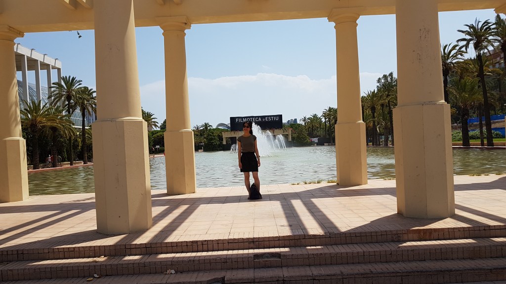 Vi in het park tussen kolommen, met palmbonen en een fontein op de achtergrond.