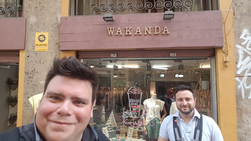 Javi en ik staan voor een winkel met een houten uithangbord. De winkel heet Wakanda.