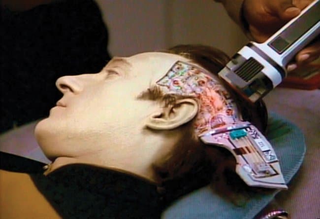 Android en kunstmatige intelligentie Data from Star Trek: The Next Generation ligt met een deel van zijn hoofd opengeklapt. LEDjes, draden en circuits zijn zichtbaar. Met futoristisch uitziend gereedschap wordt Data benaderd via een complexe gebruikersinterface.