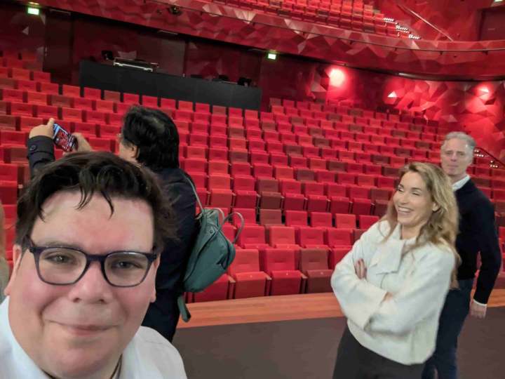 Een selfie van Randy vanaf het podium in de grote zaal van Theater Zuidplein. Op de achtergrond de rode stoelen en daarvoor UX Rotterdam initiatiefnemers Nauko en Pieter