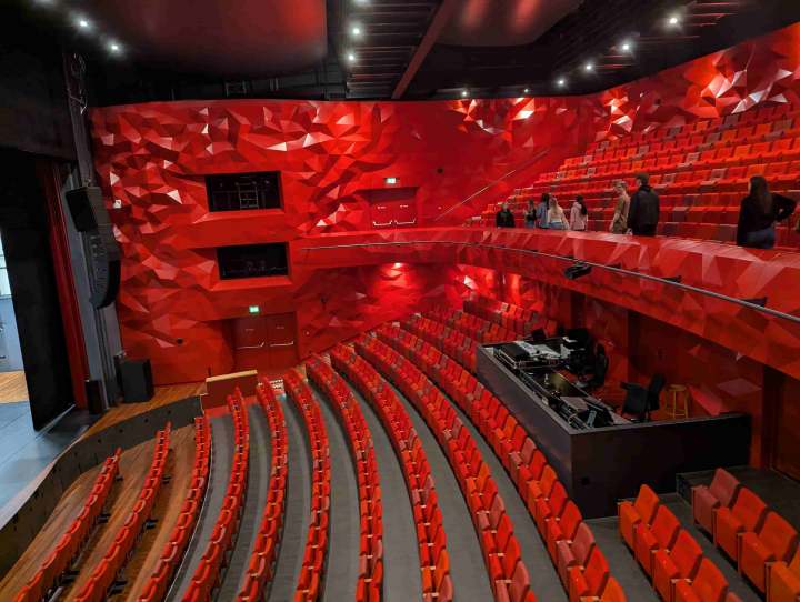 Het balkon met vrijwilligers, de rode stoelen en de rode wand met de kenmerkende facetten.